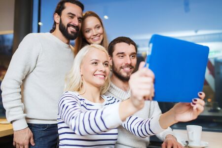 people, leisure, technology and friendship concept - happy friends with tablet pc computer taking...