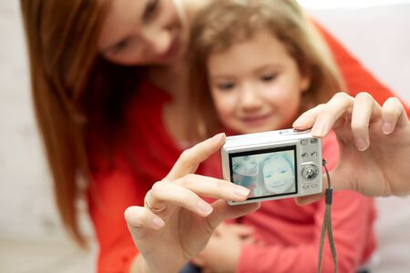 people, family and technology concept - close up of happy mother and little daughter with camera...