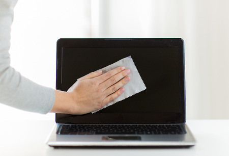 people, housework, electronics and housekeeping concept - close up of woman hand cleaning laptop...