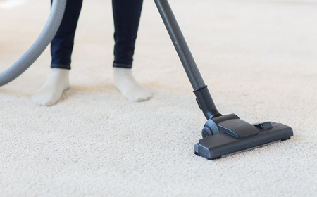 people, housework and housekeeping concept - close up of woman with legs vacuum cleaner cleaning carpet at homeの写真素材