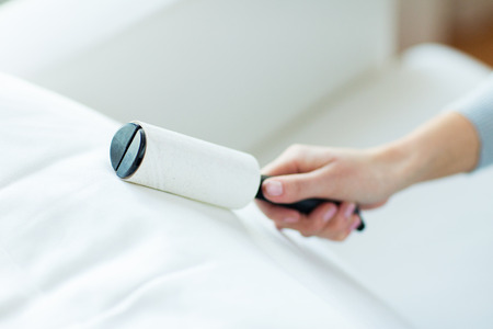 people, housework and housekeeping concept - close up of woman hand with sticky roller cleaning furniture textileの写真素材