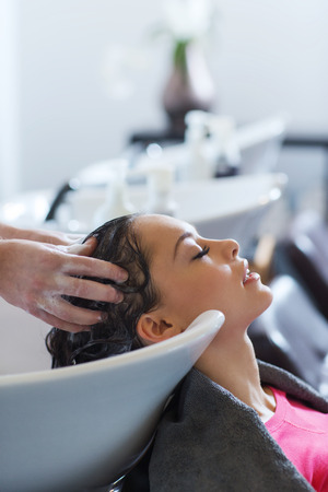 beauty and people concept - happy young woman with hairdresser washing head at hair salonの写真素材