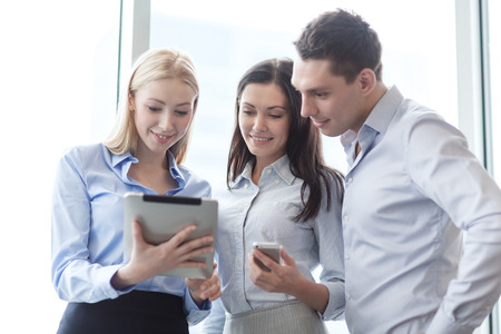 business and office concept - smiling business team working with tablet pcs and smartphones in...