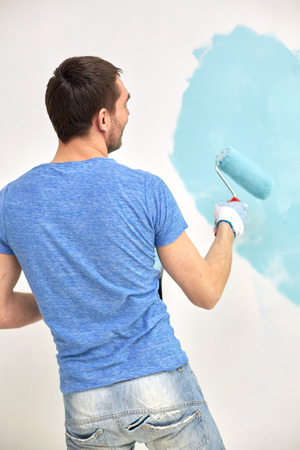 repair, building, people and renovation concept - man with roller painting wall in blue at homeの写真素材