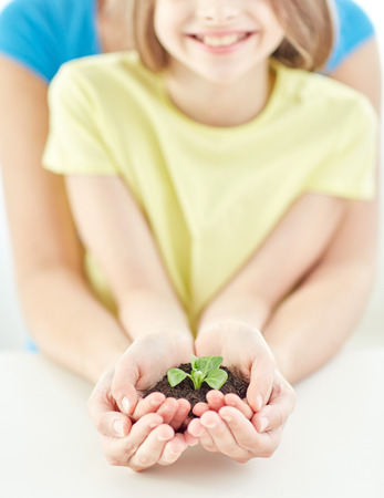 people, charity, family and ecology concept - close up of child and parent cupped hands holding soil with green sprout at homeの写真素材