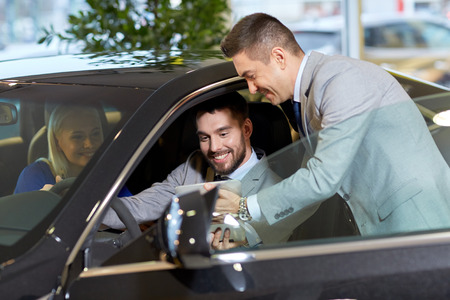 auto business, car sale, technology and people concept - happy couple with car dealer in auto show...