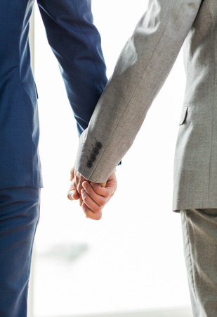 people, homosexuality, same-sex marriage and love concept - close up of happy male gay couple holding hands from backの写真素材
