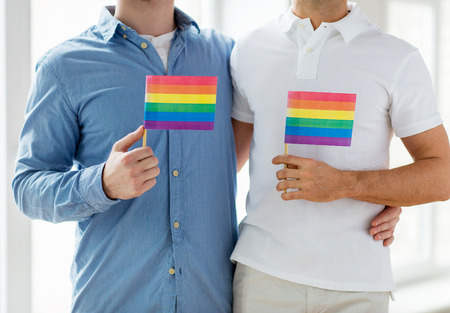 people, homosexuality, same-sex marriage, gay and love concept - close up of happy male gay couple hugging and holding rainbow flags at homeの写真素材