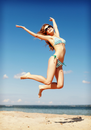 summer holidays and vacation concept - beautiful woman in bikini jumping on the beachの写真素材