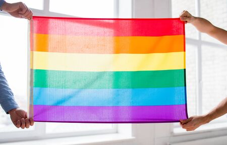 people, homosexuality, same-sex, gay and love concept - close up of happy male gay couple hugging and holding rainbow flag at homeの写真素材