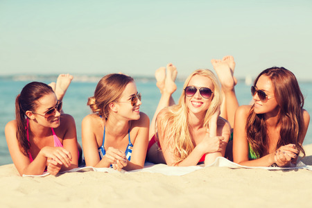 summer vacation, holidays, travel and people concept - group of smiling young women in sunglasses lying on beachの写真素材