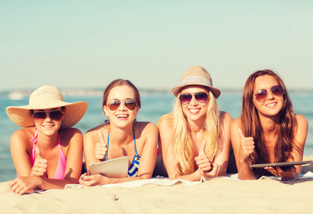 summer vacation, travel, technology and people concept - group of smiling women in sunglasses with tablet pc computers lying on beachの写真素材