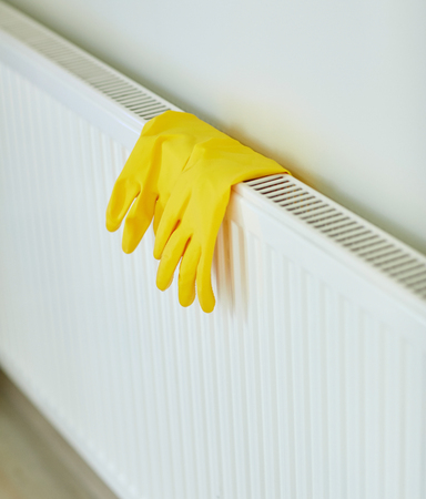 protection, housework and housekeeping concept - close up of yellow rubber gloves hanging on heater at homeの写真素材