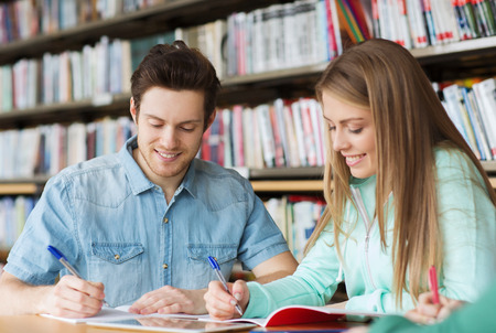 people, knowledge, education and school concept - group of happy students writing to notebooks in libraryの写真素材