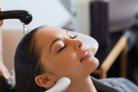 beauty and people concept - happy young woman with hairdresser washing head at hair salonの写真素材