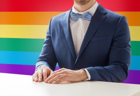 people, gay, wedding and same-sex marriage concept - close up of best man or groom in suit and bow-tie at table over rainbow flag backgroundの写真素材