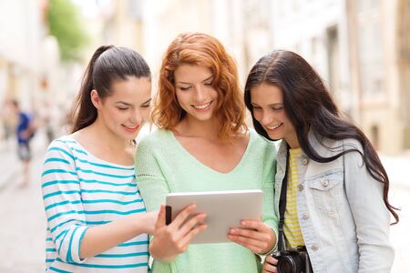 tourism, travel, leisure, holidays and friendship concept - smiling teenage girls with witch tablet pc computer and camera outdoorsの写真素材