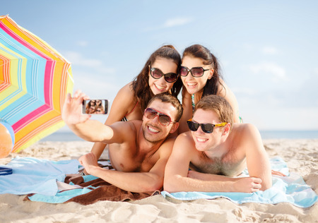 summer holidays, vacation, technology and people concept - group of happy friends taking selfie by smartphone and sunbathing on beachの写真素材