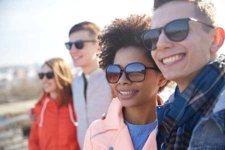 tourism, travel, people, leisure and teenage concept - group of smiling teenagers in sunglasses hugging on city streetの写真素材