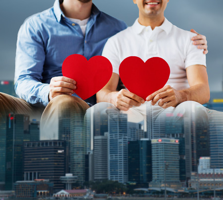 people, homosexuality, same-sex marriage, valentines day and love concept - close up of happy gay male couple with red hearts over city backgroundの写真素材