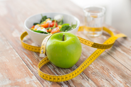 healthy eating dieting slimming and weigh loss concept  close up of green apple measuring tape and salad