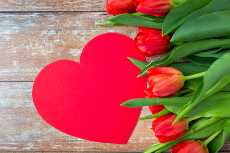 flowers advertisement valentines day and holidays concept  close up of red tulips and blank paper heart shape on wooden backgroundの写真素材