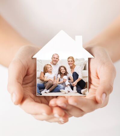 real estate, home insurance and happiness concept - close up of female hands holding white house with happy family pictureの写真素材