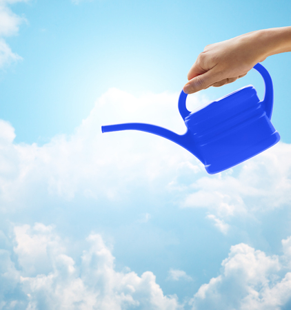 people, gardening and profession concept - close up of woman or gardener hand holding watering can over blue sky with cloudsの写真素材