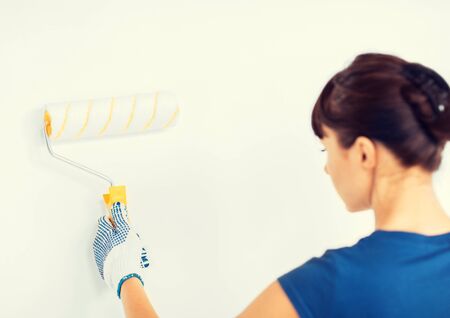 interior design and home renovation concept - woman with roller and paint colouring the wallの写真素材
