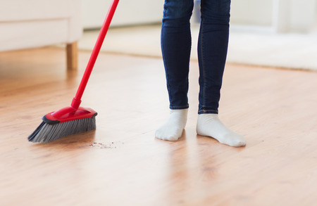 people, housework, cleaning and housekeeping concept - close up of woman legs with broom sweeping floor at homeの写真素材