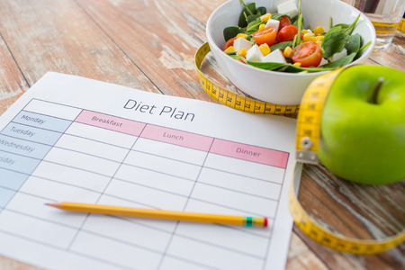 healthy eating, dieting, slimming and weigh loss concept - close up of diet plan paper green apple, measuring tape and salad healthy eating, dieting, slimming and weigh loss concept - close up of diet plan paper green apple, measuring tape and salad