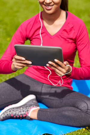 fitness, technology, people and sport concept - close up of smiling african american woman with tablet pc computer sitting on mat outdoorsの写真素材