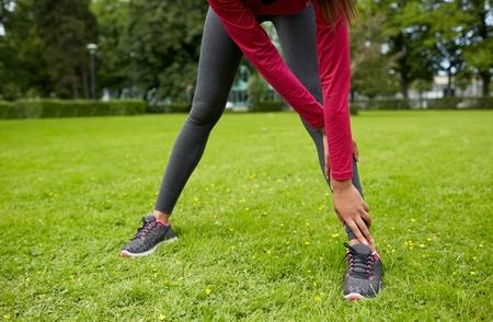 fitness, sport, training, people and lifestyle concept - close up of woman stretching leg in park