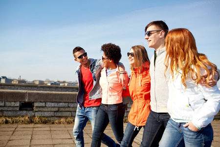 tourism, travel, people and leisure concept - group of happy teenage friends walking along city...