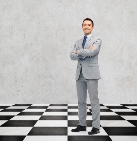 business, people and strategy concept - happy smiling businessman in suit standing on checkerboard pattern floor over gray backgroundの写真素材