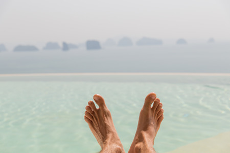 summer holidays, beach, travel, leisure and body care concept - closeup of male feet over sea and skyの写真素材