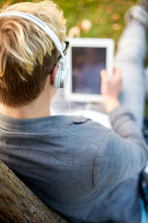close up of teenage boy in headphones with tablet pc computer listening to music online at parkの写真素材