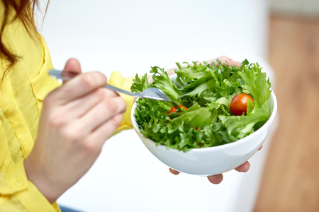 close up of young woman eating vegetable salad at homeの写真素材