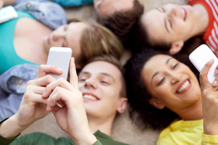 education, people and technology concept - close up of students or friends with smartphones lying on floor in circleの写真素材
