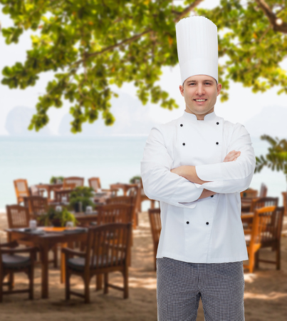 cooking, profession and people concept - happy male chef cook with crossed hands over restaurant lounge on beachの写真素材