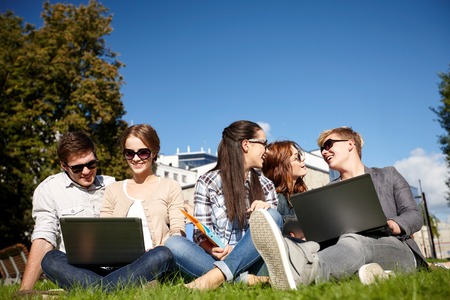 group of students or teenagers with laptop computers at park or campusの写真素材
