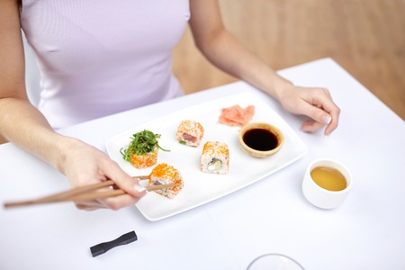 close up of woman eating sushi with chopsticks at restaurantの写真素材