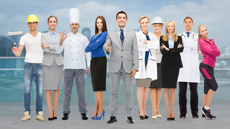 people, profession, qualification, employment and success concept - happy businessman with group of professional workers showing thumbs up over city background