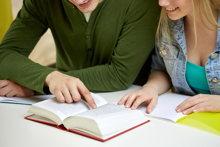 education, people and school concept - close up of happy students reading textbook or book at schoolの写真素材
