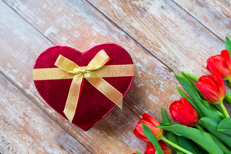 flowers, valentines day and holidays concept - close up of red tulips and heart shaped chocolate box on wooden tableの写真素材