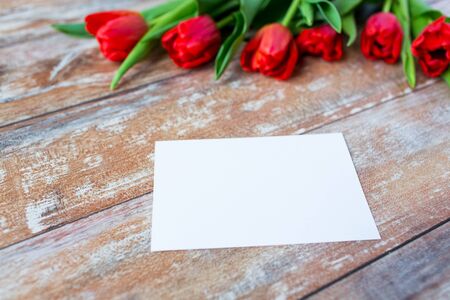 advertisement, valentines day, greeting and holidays concept - close up of red tulips and blank paper or letter on wooden backgroundの写真素材