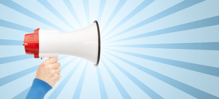 business, people and public announcement concept - close up of female hand holding megaphone over blue burst rays backgroundの写真素材