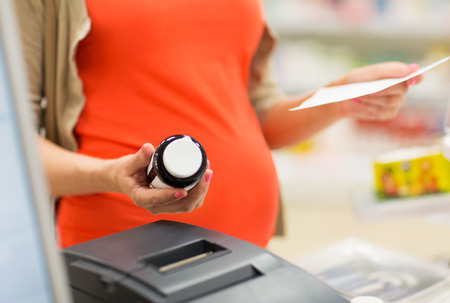 pregnancy, medicine, pharmaceutics, health care and people concept - close up of pregnant woman with prescription buying medication at pharmacy cash registerの写真素材