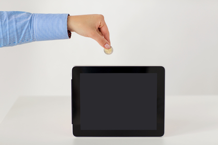 business, finance, investment, money saving and e-commerce concept - close up of hand putting coin into into tablet pc computer with black blank screenの写真素材