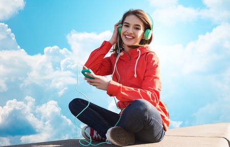 technology, music and people concept - smiling young woman or teenage girl with smartphone and...